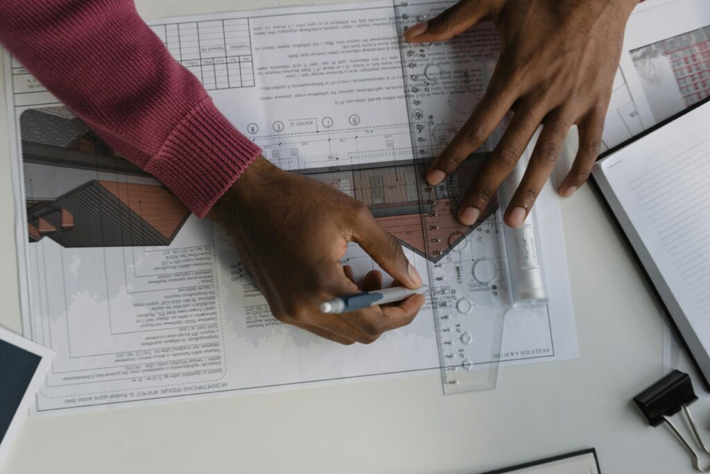 Architect sketching on blueprints with ruler at desk, designing a building layout.